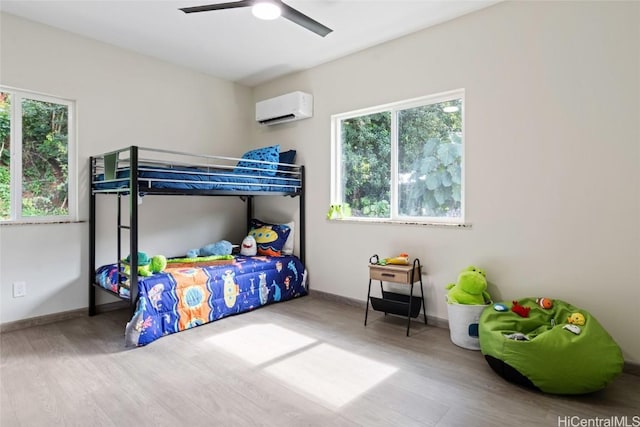 bedroom with a ceiling fan, a wall mounted air conditioner, baseboards, and wood finished floors