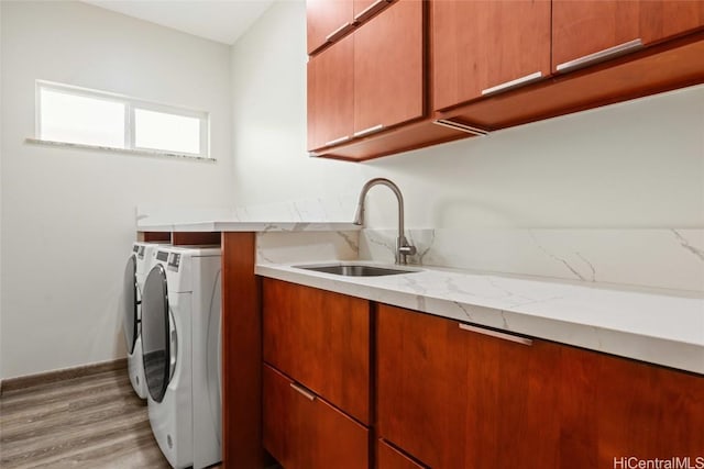 washroom with cabinet space, a sink, separate washer and dryer, light wood-type flooring, and baseboards