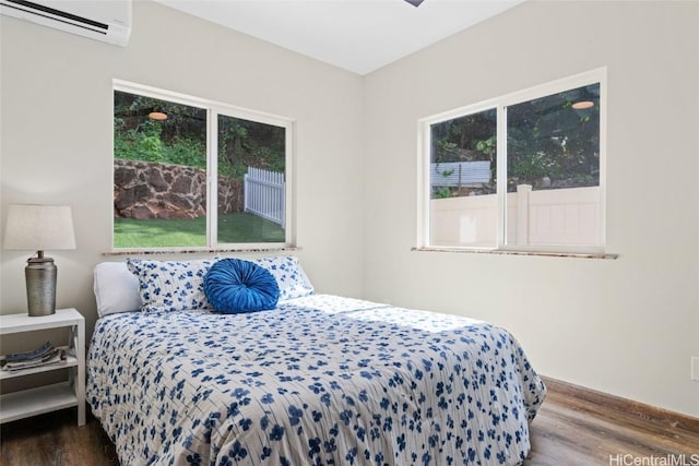 bedroom with multiple windows, a wall unit AC, and wood finished floors