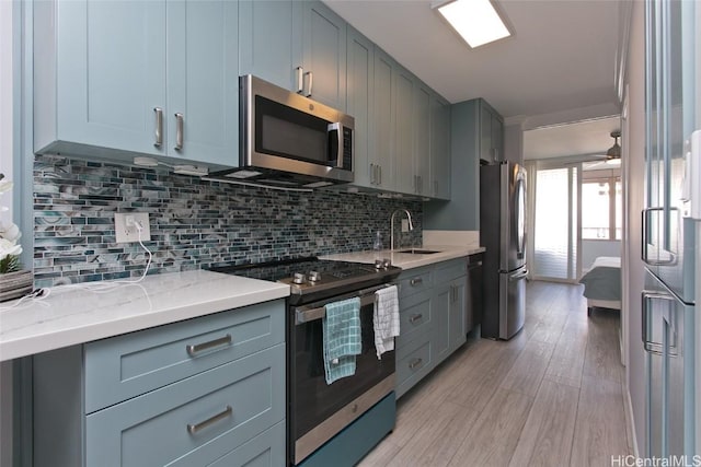 kitchen featuring light wood-style flooring, gray cabinetry, stainless steel appliances, a sink, and tasteful backsplash