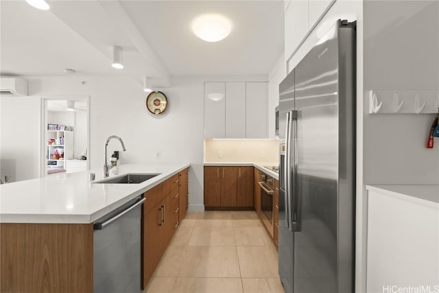 kitchen with brown cabinetry, a peninsula, stainless steel appliances, a sink, and a wall mounted AC