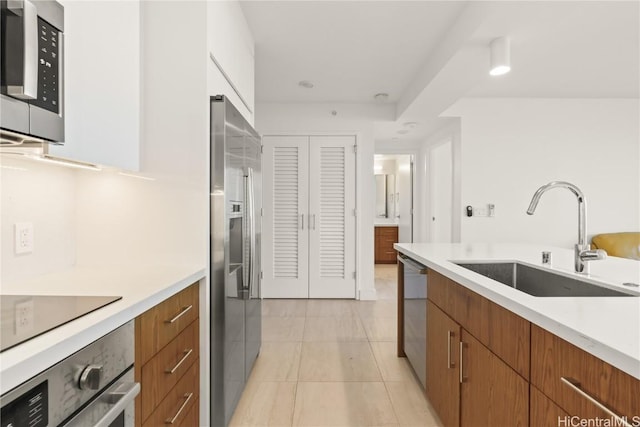 kitchen featuring appliances with stainless steel finishes, brown cabinets, light countertops, and a sink