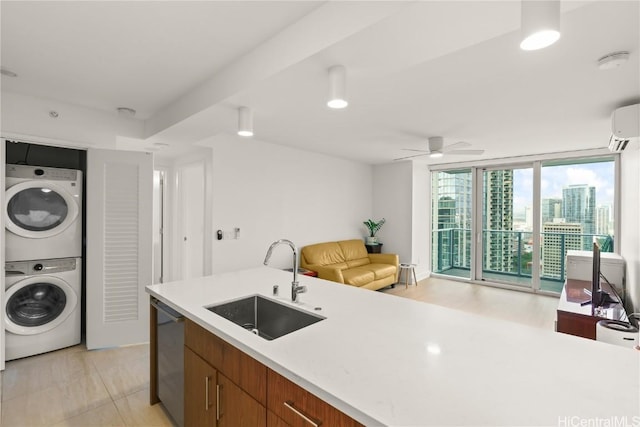 kitchen featuring a sink, light countertops, stainless steel dishwasher, stacked washing maching and dryer, and a wall of windows