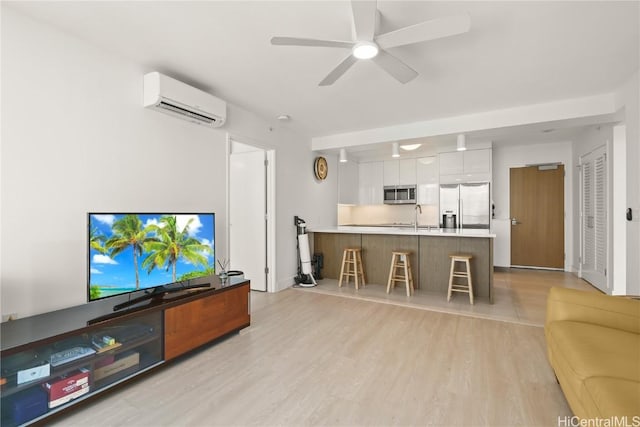 living room with a wall unit AC, light wood-style floors, and a ceiling fan