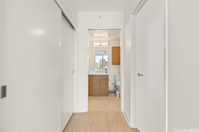 corridor featuring light wood-type flooring and a sink