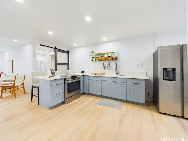 kitchen featuring a barn door, a peninsula, stainless steel appliances, light countertops, and a sink