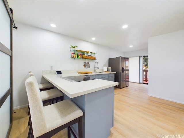 kitchen with gray cabinets, light countertops, stainless steel fridge, a peninsula, and a kitchen bar