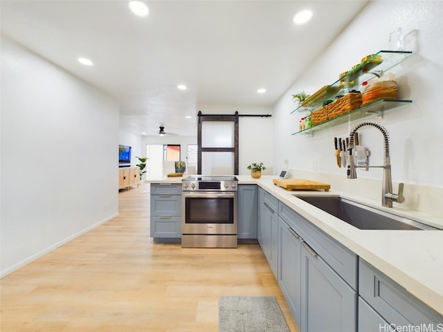 kitchen featuring light countertops, a barn door, light wood-style floors, a sink, and stainless steel electric range