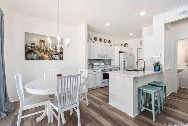 kitchen with white appliances, a sink, white cabinetry, a kitchen breakfast bar, and dark wood finished floors