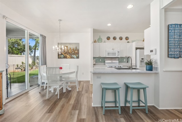 kitchen featuring light wood finished floors, decorative backsplash, a sink, white appliances, and a peninsula