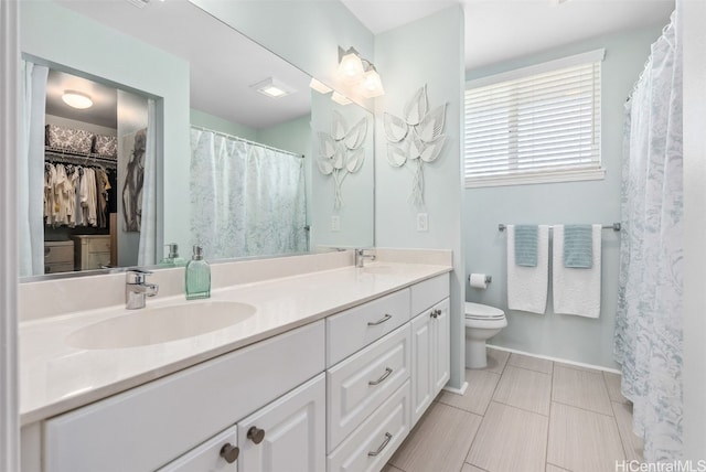 bathroom featuring double vanity, a spacious closet, a sink, and toilet