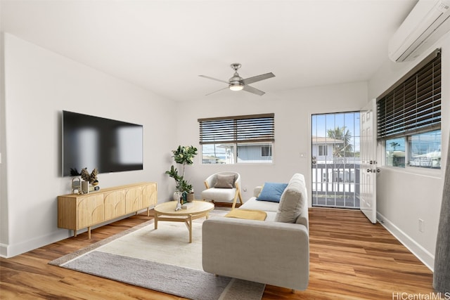 living room with an AC wall unit, a ceiling fan, baseboards, and wood finished floors