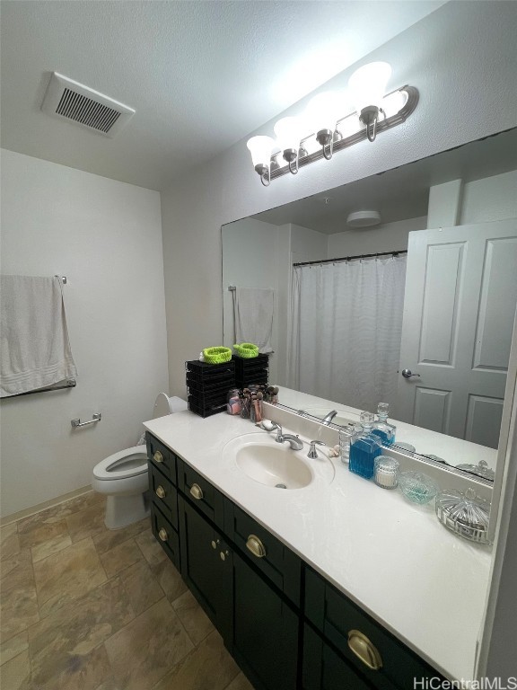 full bath featuring stone finish flooring, visible vents, vanity, and toilet