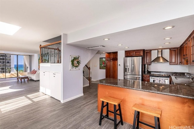 311 Ohua Ave Unit Ph D, Honolulu, HI 96815 - kitchen with dark stone countertops, wood finished floors, a peninsula, appliances with stainless steel finishes, and wall chimney range hood