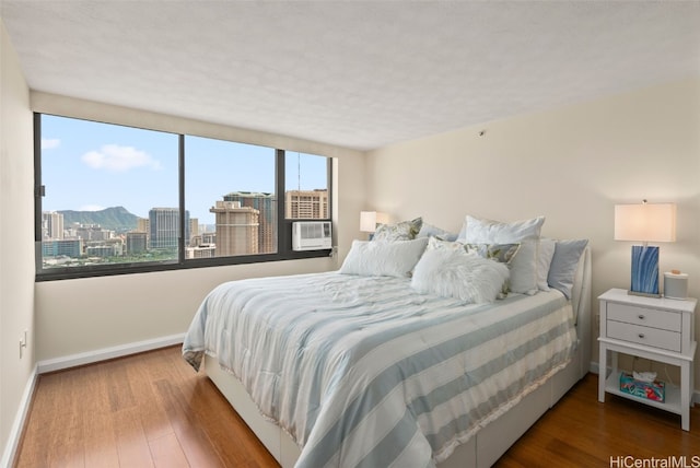 bedroom with baseboards, cooling unit, wood finished floors, and a city view