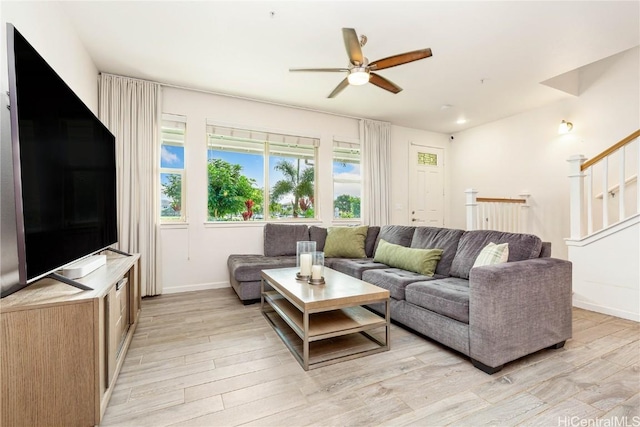 living area featuring a ceiling fan, stairway, light wood-style flooring, and baseboards