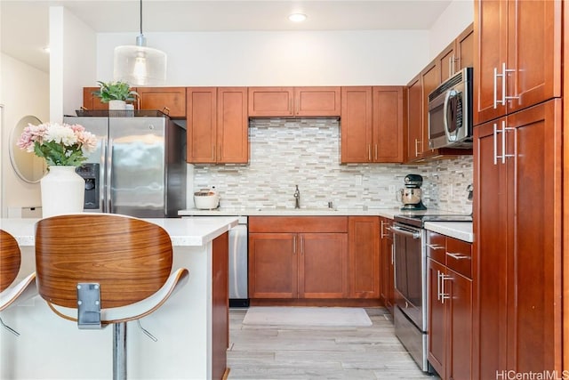 kitchen featuring light wood-style floors, light countertops, appliances with stainless steel finishes, tasteful backsplash, and pendant lighting