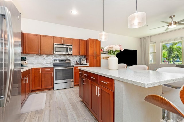 kitchen featuring tasteful backsplash, light wood-style flooring, appliances with stainless steel finishes, decorative light fixtures, and a kitchen bar