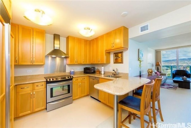 kitchen with a peninsula, stainless steel appliances, a sink, light countertops, and wall chimney exhaust hood