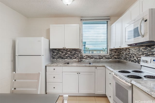 kitchen with white appliances, tasteful backsplash, light tile patterned floors, white cabinetry, and a sink