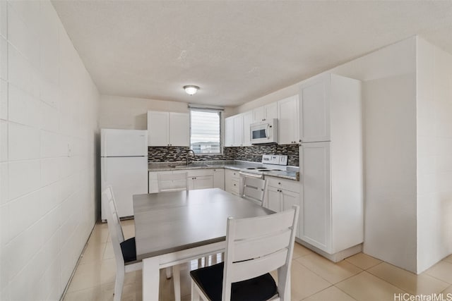 kitchen with light tile patterned floors, tasteful backsplash, white cabinets, a sink, and white appliances