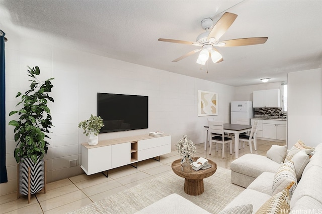 living room featuring light tile patterned floors, ceiling fan, and a textured ceiling