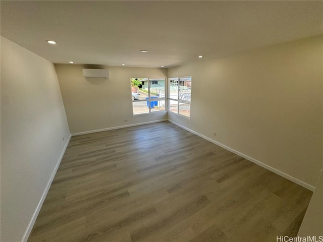 spare room featuring recessed lighting, a wall unit AC, wood finished floors, and baseboards