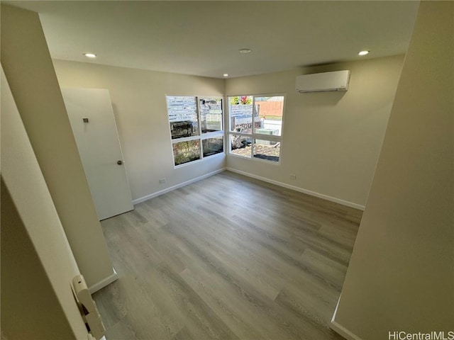 spare room featuring light wood-type flooring, baseboards, an AC wall unit, and recessed lighting