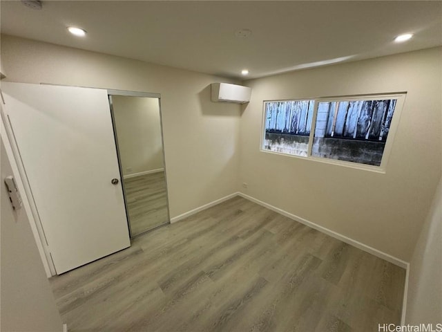 below grade area with recessed lighting, light wood-style flooring, baseboards, and a wall mounted AC