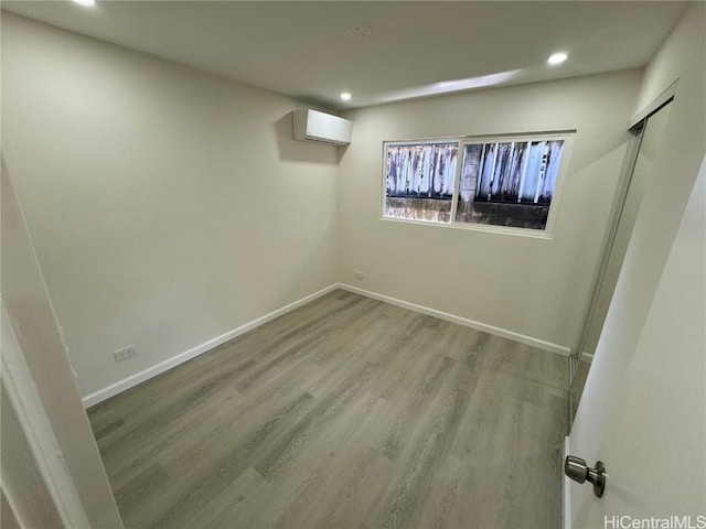 below grade area with light wood finished floors, a wall unit AC, recessed lighting, and baseboards