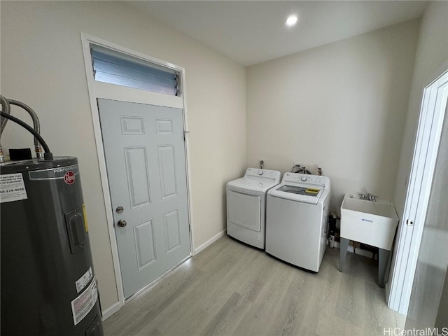 laundry room with laundry area, electric water heater, washer and dryer, light wood-style floors, and a sink