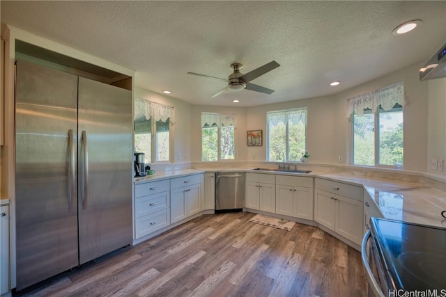 kitchen with white cabinets, appliances with stainless steel finishes, wood finished floors, light countertops, and a sink