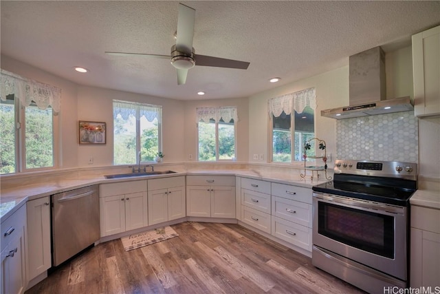 kitchen featuring light countertops, appliances with stainless steel finishes, a sink, light wood-type flooring, and wall chimney exhaust hood