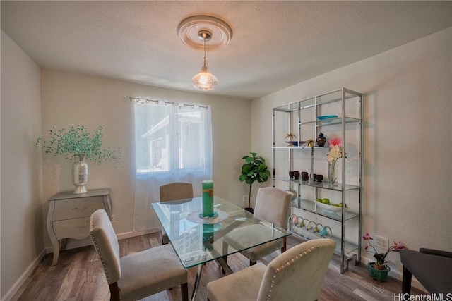 dining area featuring a textured ceiling, wood finished floors, and baseboards