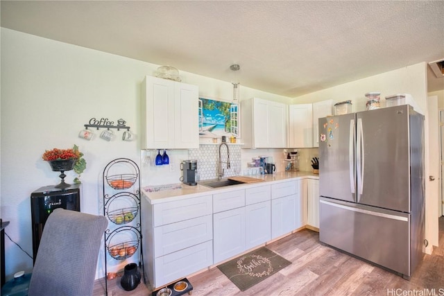 kitchen featuring light wood-style flooring, a sink, white cabinetry, freestanding refrigerator, and tasteful backsplash