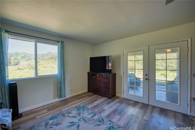 interior space featuring french doors, a textured ceiling, baseboards, and wood finished floors