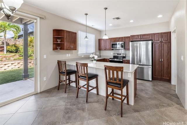 kitchen with stainless steel appliances, light countertops, visible vents, hanging light fixtures, and a peninsula