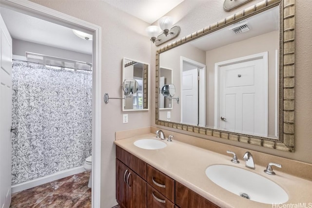 bathroom featuring toilet, double vanity, visible vents, and a sink