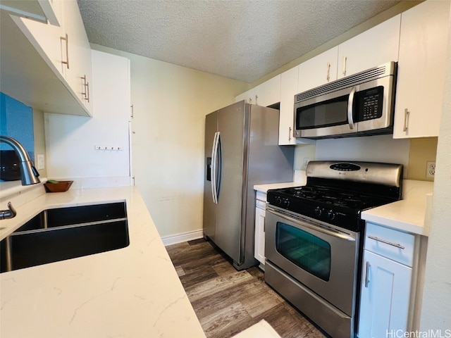 kitchen featuring a textured ceiling, stainless steel appliances, a sink, and dark wood finished floors