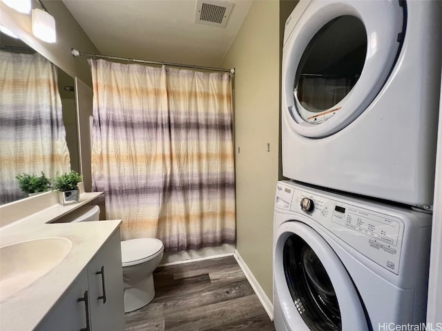 bathroom featuring stacked washer and dryer, visible vents, toilet, wood finished floors, and vanity