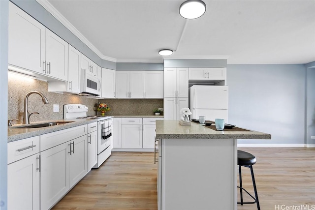 kitchen featuring white appliances, tasteful backsplash, a breakfast bar, a center island, and a sink