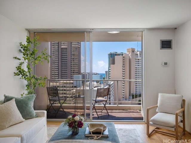 living area with a city view, visible vents, floor to ceiling windows, and wood finished floors