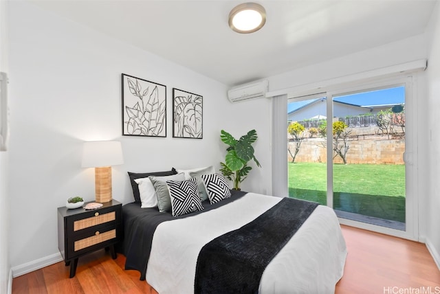 bedroom featuring access to exterior, baseboards, wood finished floors, and a wall mounted AC