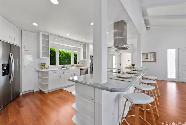 kitchen featuring light wood finished floors, lofted ceiling with beams, appliances with stainless steel finishes, a kitchen breakfast bar, and island exhaust hood