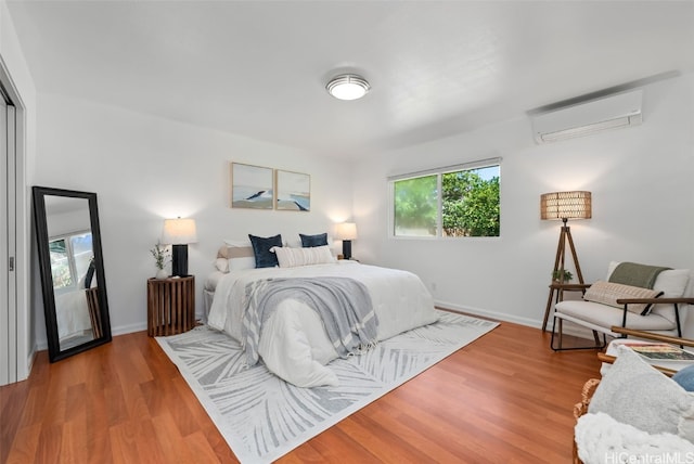 bedroom with a wall unit AC, baseboards, and wood finished floors