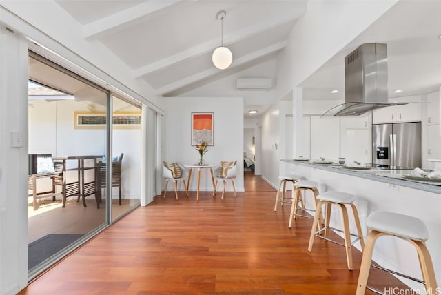 kitchen with lofted ceiling with beams, a breakfast bar, a wall mounted AC, stainless steel fridge with ice dispenser, and island exhaust hood