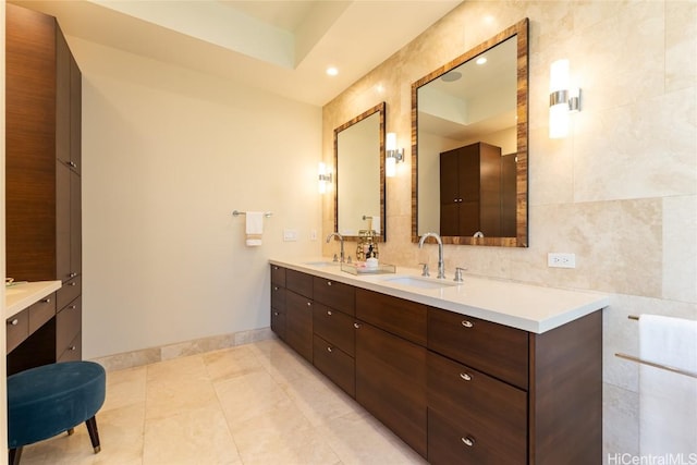 full bath with double vanity, a sink, tile walls, and baseboards