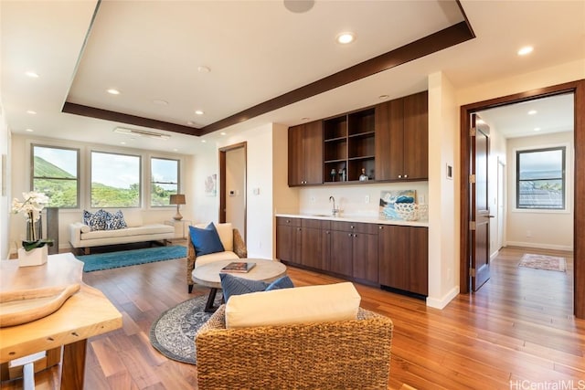 living area featuring light wood-style floors, recessed lighting, a raised ceiling, and baseboards