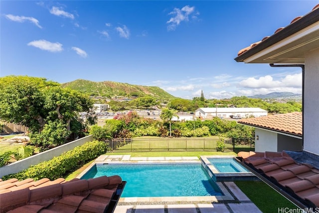 view of pool featuring a pool with connected hot tub, a fenced backyard, a mountain view, and a lawn