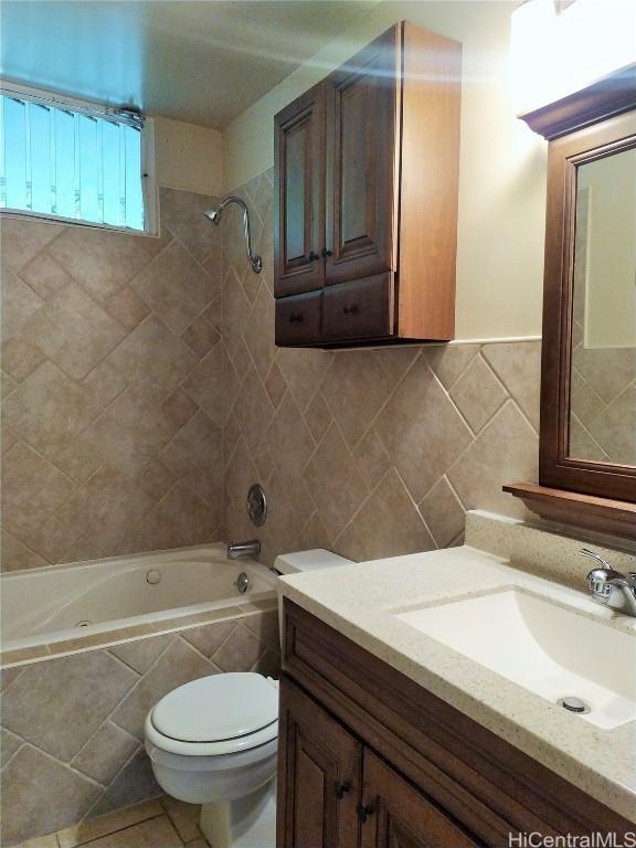 bathroom with tiled shower / bath combo, toilet, tile walls, and vanity